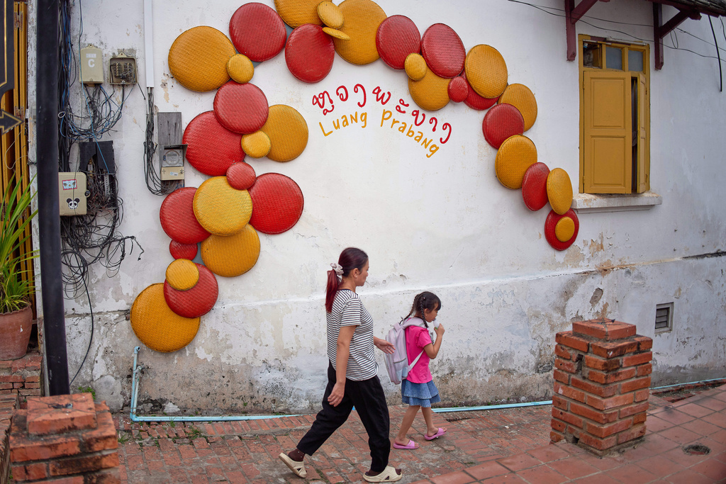 Locals walk past a decorated wall in the UNESCO World Heritage city of Luang Prabang, Laos Wednesday, Nov. 5, 2025. (AP Photo/Eugene Hoshiko)