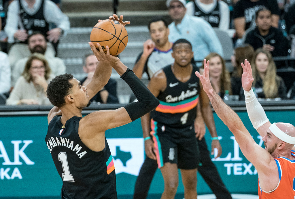 San Antonio Spurs forward Victor Wembanyama (1) hits a three point shot over Oklahoma Thunder guard Alex Caruso (9) during the second half of an NBA basketball game in San Antonio, Tuesday, Dec. 23, 2025. (AP Photo/Rodolfo Gonzalez)