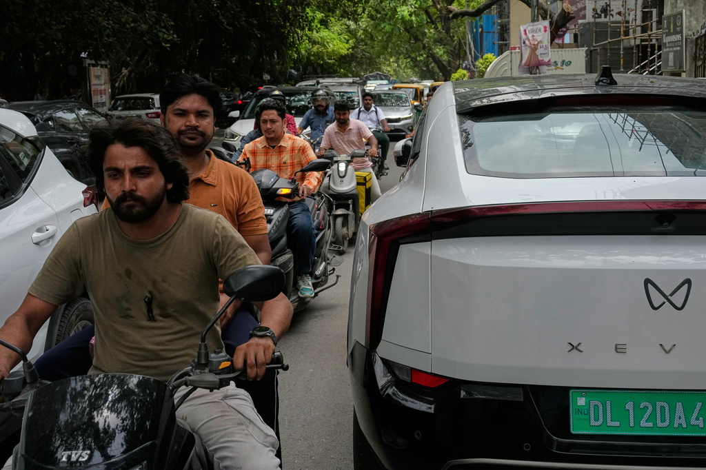Two wheelers drive past an electric vehicle parked along a street in New Delhi, India, Monday, July 13, 2026. (AP Photo/Manish Swarup)