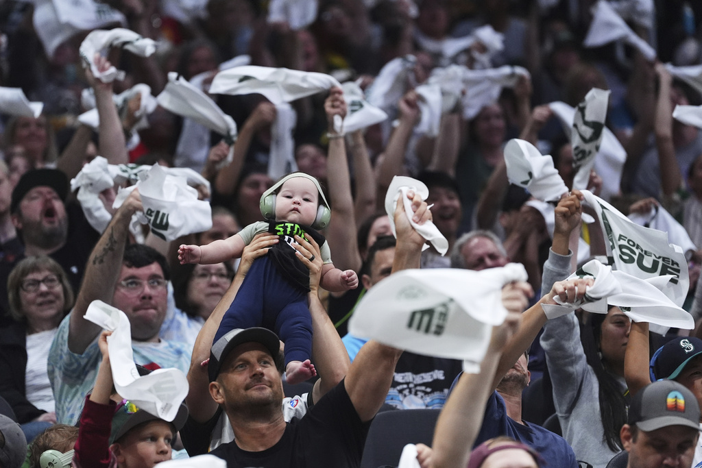 A fan holds up their baby as others wave towels during a Phoenix Mercury free throw against the Seattle Storm during the first half of a WNBA basketball game Sunday, Aug. 17, 2025, in Seattle. (AP Photo/Lindsey Wasson)