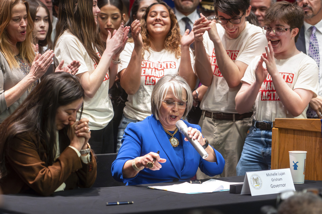 FILE - Gov. Michelle Lujan Grisham, center, prepares to sign House Bill 129, as bill co-sponsor Rep. Andrea Romero, D-Santa Fe, left, clasps her hands at West Mesa High School in Albuquerque, N.M., March 4, 2024. (Jon Austria/The Albuquerque Journal via AP, File)