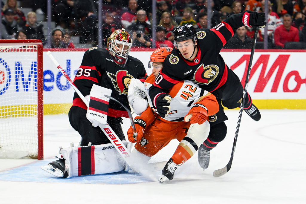 Ottawa Senators' Jordan Spence (10) crashes into Anaheim Ducks' Tim Washe (42) in front Senators' goaltender Linus Ullmark (35) during the first period of an NHL hockey game, Saturday, March 14, 2026, in Ottawa, Ontario. (Spencer Colby/The Canadian Press via AP)