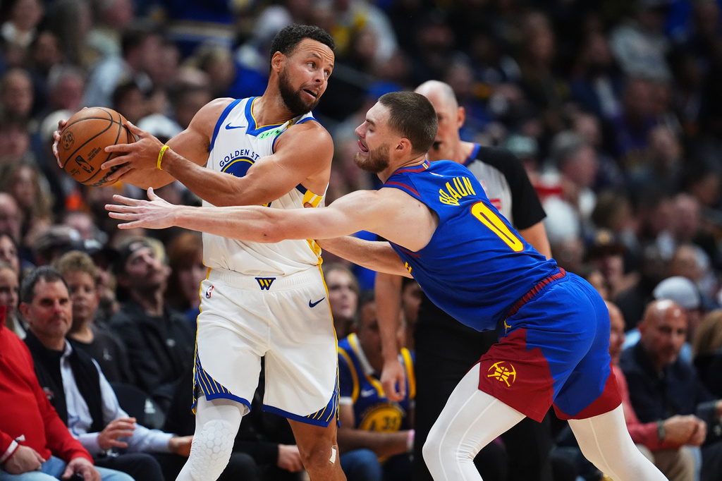 Golden State Warriors guard Stephen Curry, left, looks to pass the ball while under pressure from Denver Nuggets guard Christian Braun, right, in the first half of an NBA basketball game Monday, Oct. 26, 2026, in Denver. (AP Photo/David Zalubowski)