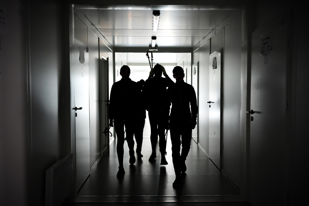 Biathletes Yekateryna Mashtalier, 18, Mykola Dorofeiev, 16, Maksym Kravchenko, 17, and Nazar Kravchenko, 12, walk through a dark hallway during a blackout at their mobile gym outside the destroyed ski base in Chernihiv, Ukraine, Thursday, Oct. 30, 2025. (AP Photo/Julia Demaree Nikhinson)