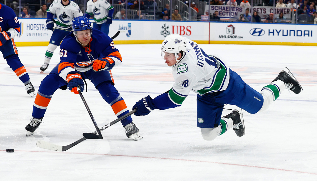 Vancouver Canucks left wing Drew O'Connor (18) shoots against New York Islanders Emil Heineman (51) during the first period of an NHL hockey game, Friday, Dec. 19, 2025, in Elmont, N.Y. (AP Photo/Noah K. Murray)