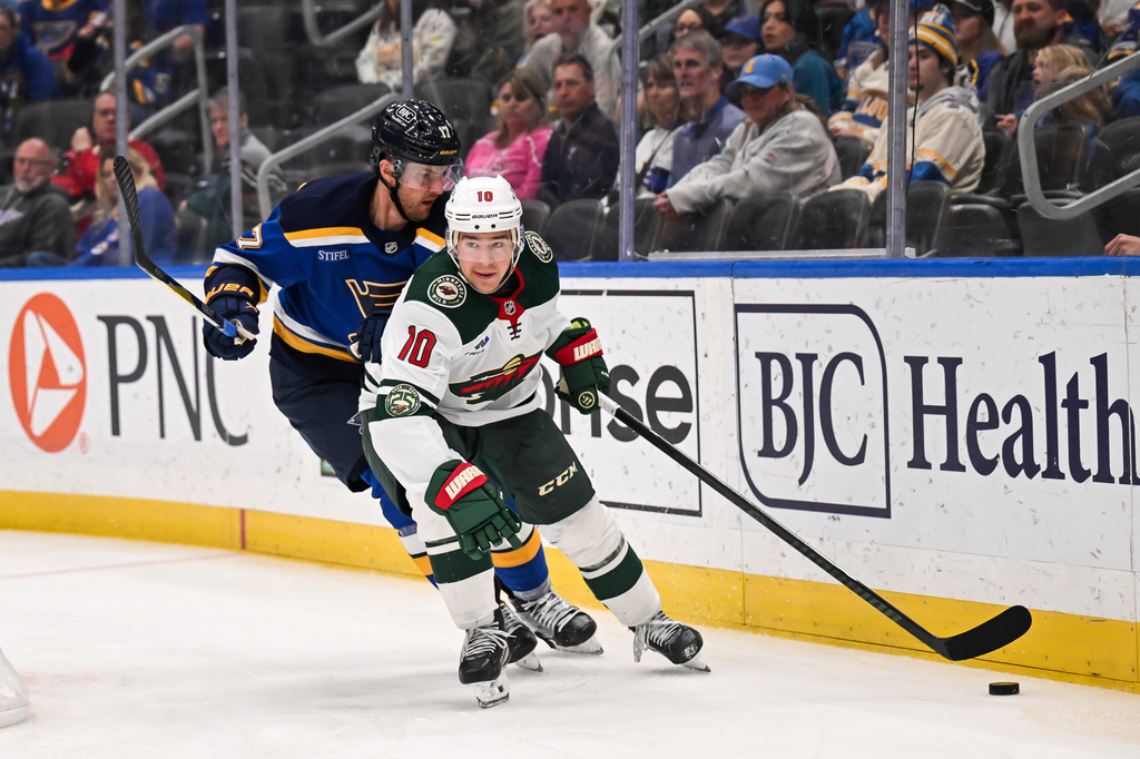Minnesota Wild's Bobby Brink (10) controls the puck while under pressure from St. Louis Blues' Cam Fowler, left, during the third period of an NHL hockey game Monday, April 13, 2026, in St. Louis. (AP Photo/Connor Hamilton)