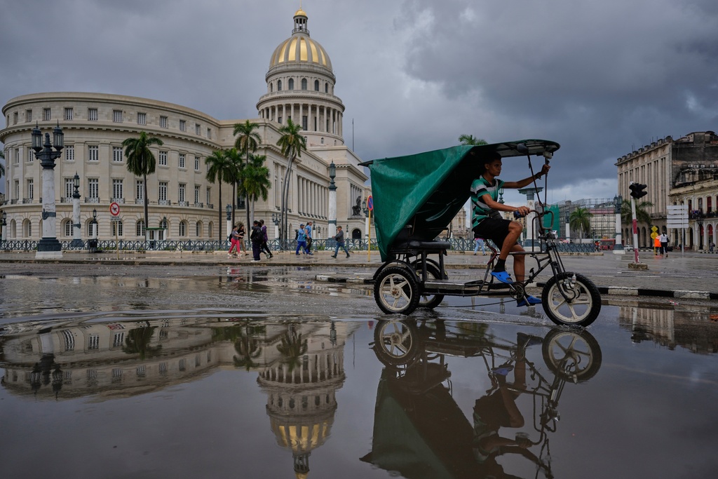 A bicycle taxi driver crosses a puddle reflecting the Capitolio, the headquarters of Parliament, in Havana, Cuba, Monday, Jan. 12, 2026. (AP Photo/Ramon Espinosa)