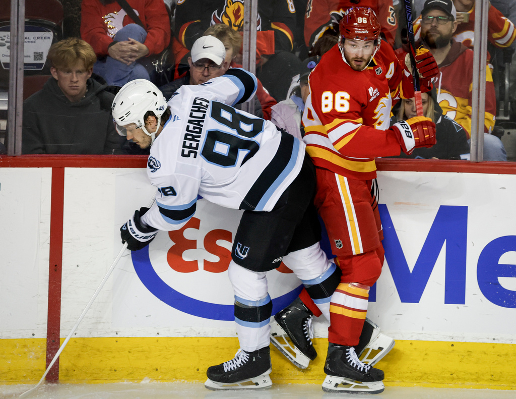 Utah Mammoth's Mikhail Sergachev, left, checks Calgary Flames' Joel Farabee during the third period of an NHL hockey game in Calgary on Sunday, April 12, 2026. (Jeff McIntosh/The Canadian Press via AP)
