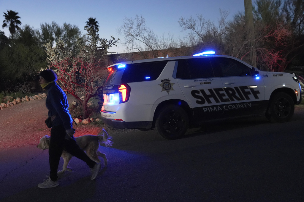 A woman walks her dog past a Pima county sheriff's vehicle parked in front of Nancy Guthrie's home on Tuesday, Feb. 10, 2026 in Tucson, Ariz. (AP Photo/Ty ONeil)