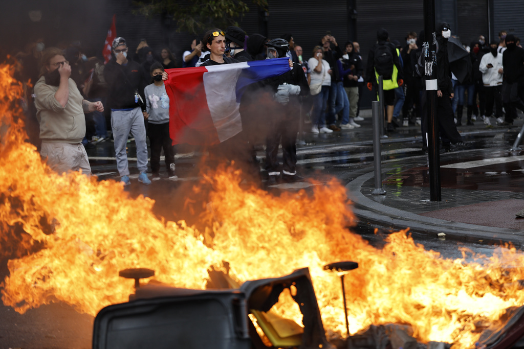 A protester of the "Block Everything" movement displays a French national flag next to burning cabbage bins in Lille, northern France, Wednesday, Sept. 10, 2025. (AP Photo/Jean-Francois Badias)