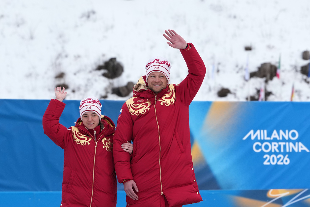 Anastasiia Bagiian, of Russia, and her guide Sergei Siniakin, wave from the podium after winning the gold medal in the cross country skiing women's 10Km interval start classic vision impaired final at the 2026 Winter Paralympics, in Tesero, Italy, Wednesday, March 11, 2026. (AP Photo/Evgeniy Maloletka)