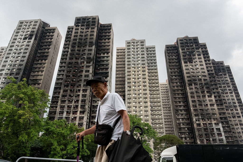 FILE -A person walks past fire-ravaged residential towers of the Wang Fuk Court apartment complex after the deadly fire in November, in the Tai Po district of Hong Kong, April 20, 2026. (AP Photo/Chan Long Hei, File)