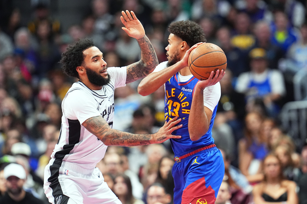 Denver Nuggets forward Cameron Johnson, right, looks to pass the ball as San Antonio Spurs forward Julian Champagnie, left, defends in the first half of an NBA Cup basketball game Friday, Nov. 28, 2025, in Denver. (AP Photo/David Zalubowski)