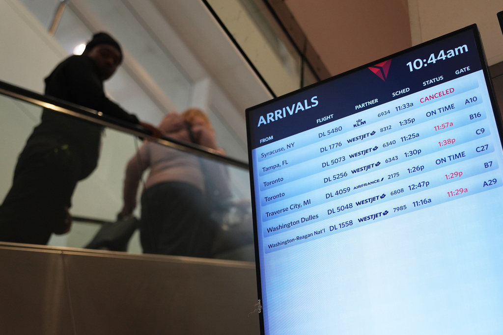 Travelers walk past a video board at the Detroit Metropolitan Airport, Sunday, Nov. 9, 2025, in Detroit. (AP Photo/Ryan Sun)