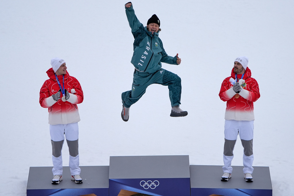 Brazil's Lucas Pinheiro Braathen, center, winner of an alpine ski, men's giant slalom race, jumps in celebration on the podium flanked by second-place Switzerland's Marco Odermatt, left, and third-place Switzerland's Loic Meillard, at the 2026 Winter Olympics, in Bormio, Italy, Feb. 14, 2026. (AP Photo/John Locher, File)