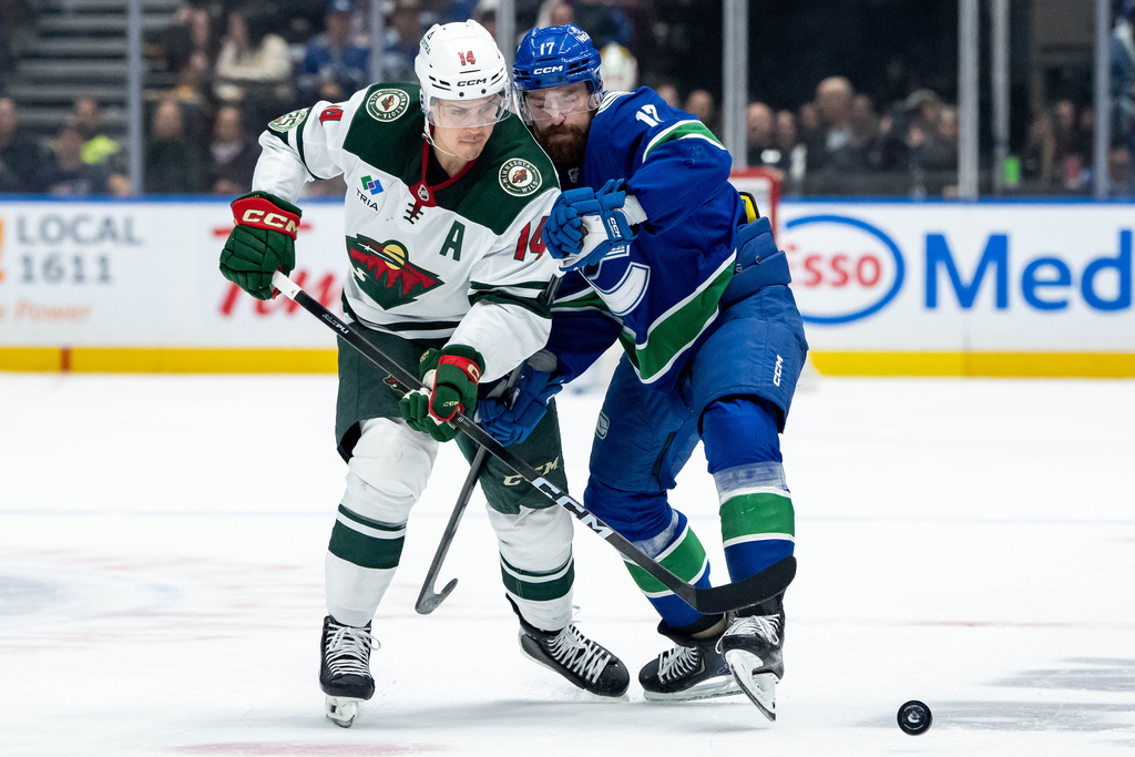 Minnesota Wild Joel Eriksson Ek (14) and Vancouver Canucks Filip Hronek (17) battle for the puck during second period NHL hockey action in Vancouver on Saturday, Dec. 6, 2025. (Ethan Cairns/The Canadian Press via AP)