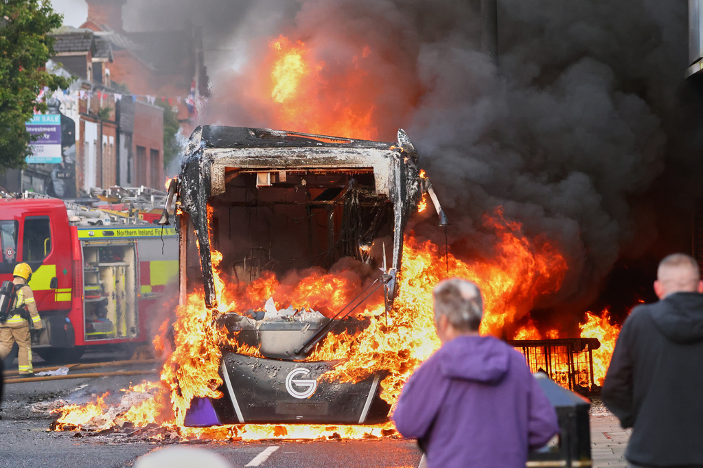 People watch as firemen arrive to put out vehicle that was set alight during a protest in East Belfast following a stabbing incident in Belfast, Tuesday, June 9, 2026. (AP Photo/Peter Morrison)