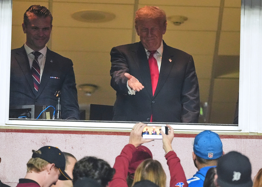 President Donald Trump, right, gestures to the crowd alongside Defense Secretary Pete Hegseth as they attend an NFL football game between the Washington Commanders and the Detroit Lions at Northwest Stadium in Landover, Md., Sunday, Nov. 9, 2025. (AP Photo/Jacquelyn Martin)