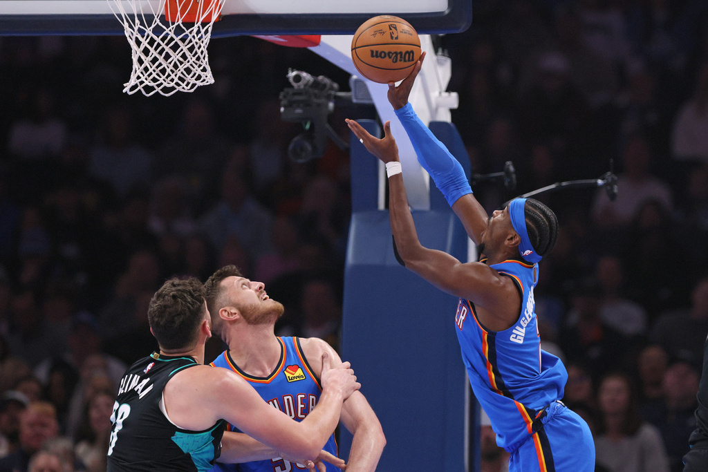 Oklahoma City Thunder guard Shai Gilgeous-Alexander, right, shoots next to Portland Trail Blazers center Donovan Clingan, left, and Thunder center Isaiah Hartenstein during the first half of an NBA basketball game, Sunday, Nov. 23, 2025, in Oklahoma City. (AP Photo/Nate Billings)