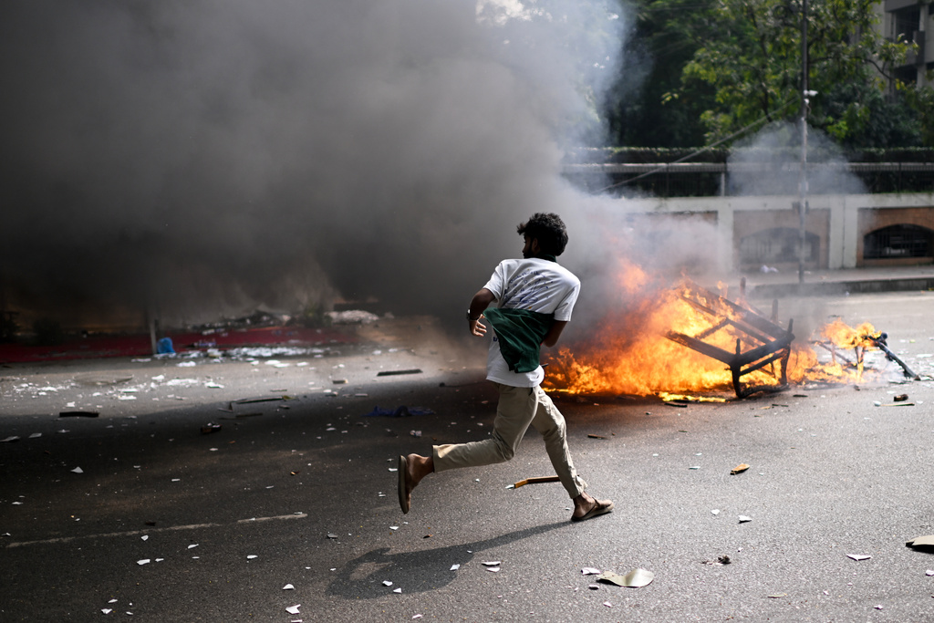 A protester runs next to burning debris from a kiosk outside Bangladesh's national parliament complex in Dhaka, Bangladesh, Friday, Oct. 17, 2025. (AP Photo/Mahmud Hossain Opu)