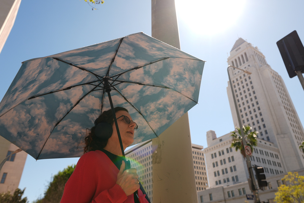 A pedestrian holds a cloud themed umbrella under a sunny day next to Los Angeles City Hall in Los Angeles Thursday, March. 12, 2026. (AP Photo/Damian Dovarganes)