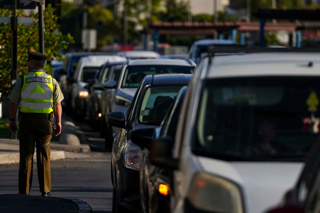 A police officer directs drivers lining up to fill their tanks with fuel in Santiago, Chile, Tuesday, March 24, 2026. (AP Photo/Esteban Felix)