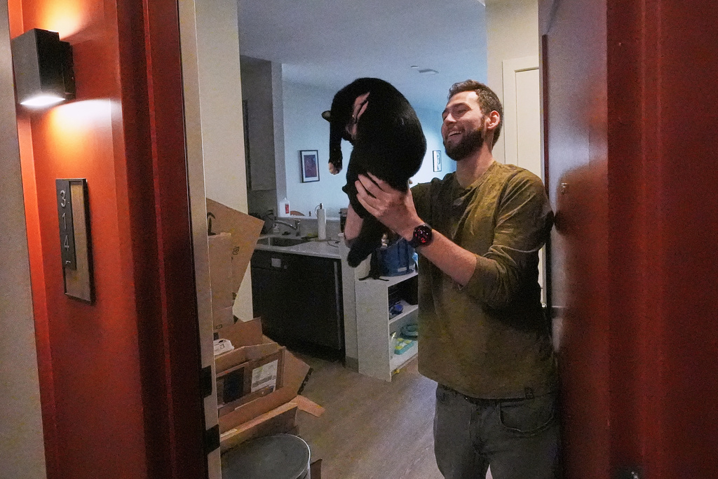Austin Geary holds up his cat, Jojo, who greeted him at his apartment door, at the Pok Oi Residences, Oct. 17, 2025, in the Chinatown neighborhood of Boston. (AP Photo/Charles Krupa)