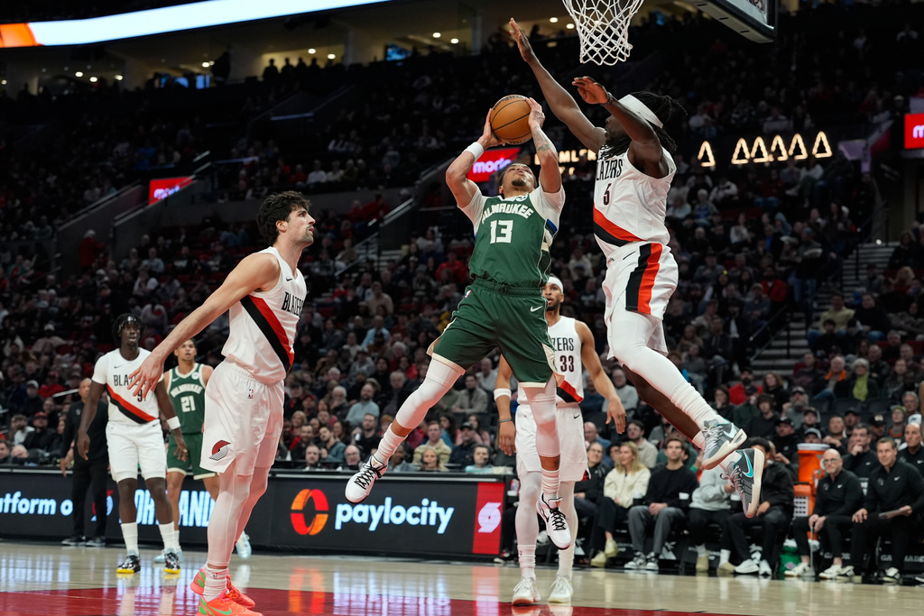 Milwaukee Bucks guard Ryan Rollins (13) goes to the basket past Portland Trail Blazers guard Jrue Holiday (5) during the first half of an NBA basketball game Wednesday, March 25, 2026, in Portland, Ore. (AP Photo/Jenny Kane)