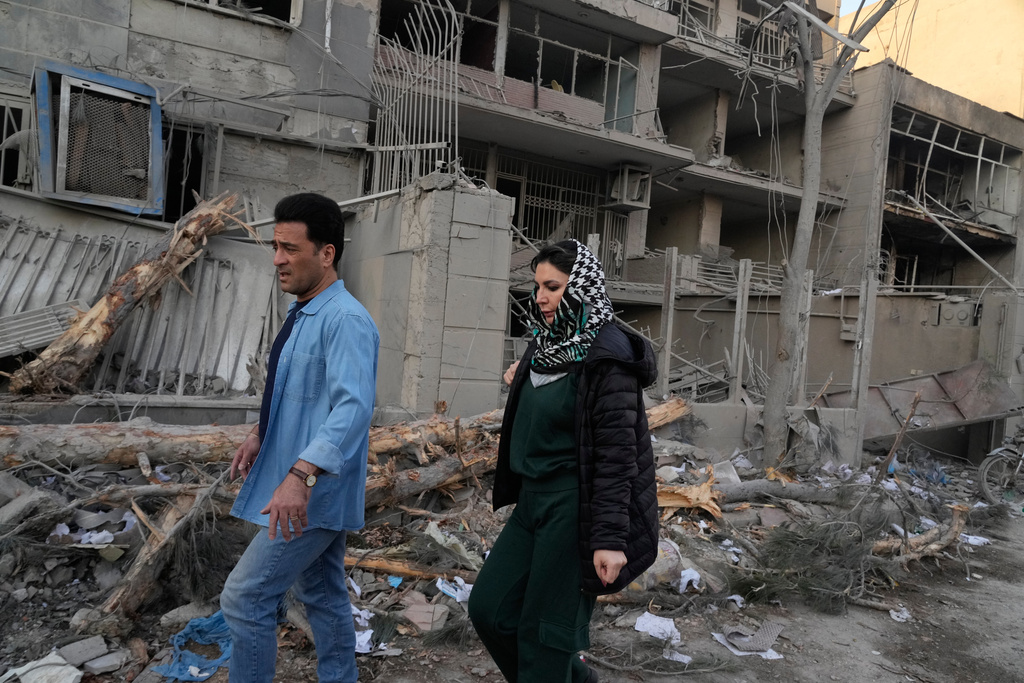 People walk past buildings damaged during a strike on a police station during ongoing, joint U.S.-Israeli military attacks in Tehran, Iran, Monday, March 2, 2026. (AP Photo/Vahid Salemi)