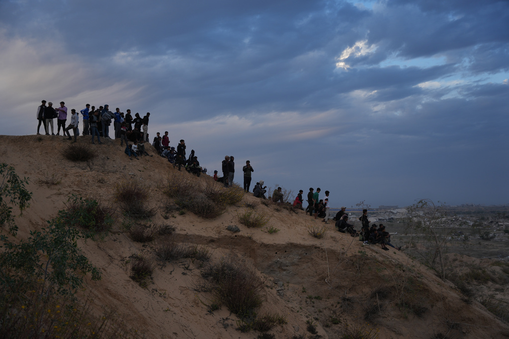 Palestinians watch youths riding their motorcycles on sand dunes in the Al-Zahra area, in the central Gaza Strip, Friday, Dec. 5, 2025. (AP Photo/Abdel Kareem Hana)