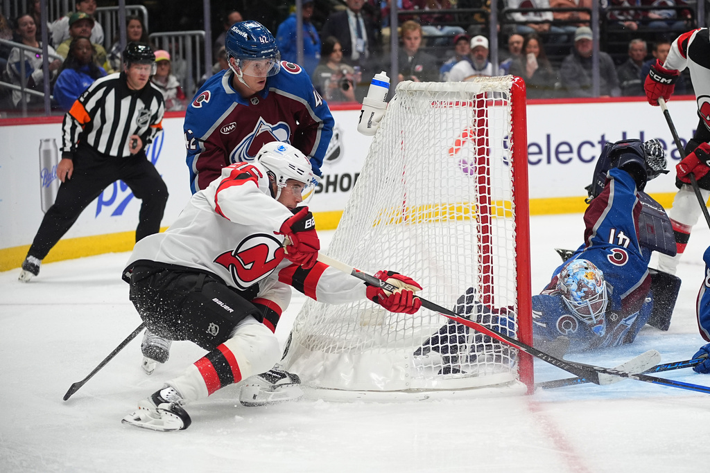 New Jersey Devils center Jack Hughes, front left, wraps around the net past Colorado Avalanche defenseman Josh Manson, back left, to put a shot on goaltender Scott Wedgewood in the second period of an NHL hockey game Tuesday, Oct. 28, 2025, in Denver. (AP Photo/David Zalubowski)