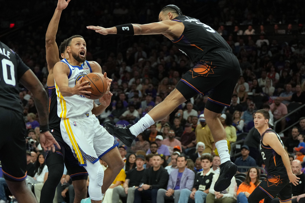 Golden State Warriors guard Stephen Curry, front left, drives against Phoenix Suns forward Dillon Brooks (3) during the first half of an NBA basketball play-in tournament game, Friday, April 17, 2026, in Phoenix. (AP Photo/Rick Scuteri)