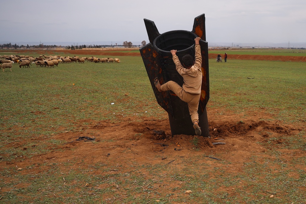 Exposing himself to the danger of unexploded ordnance, a boy tries to climb on an unexploded Iranian projectile that landed in an open field in the outskirts of Qamishli, eastern Syria, Wednesday, March 4, 2026.(AP Photo/Baderkhan Ahmad)