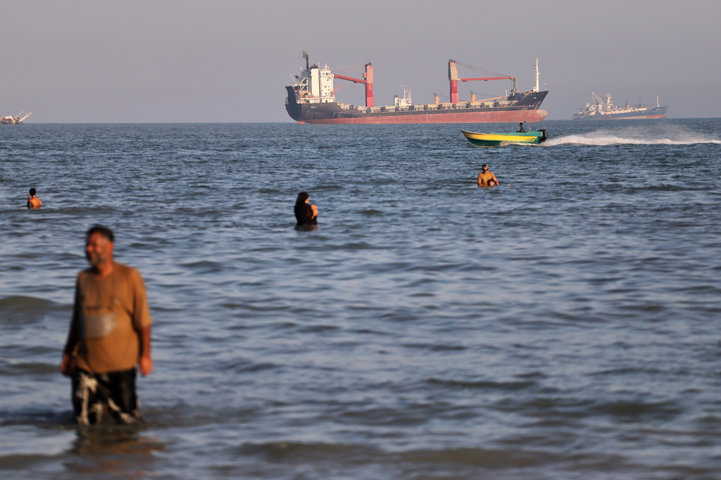 Residents swim in the waters of the Strait of Hormuz as a small motorboat passes cargo ships and other commercial vessels offshore near Bandar Abbas, Iran, Wednesday, June 17, 2026. (Amirhosein Khorgooi/ISNA via AP)