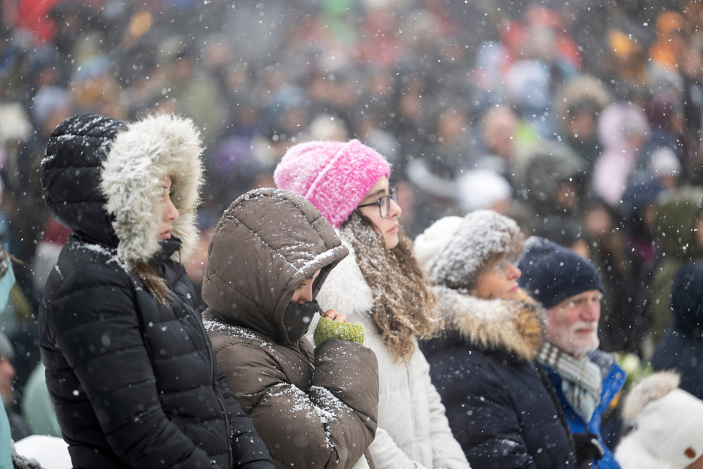 People gather to watch the official commemorative ceremony on a giant screen in front of the St. Christopher Chapel in Crans-Montana during the national day of mourning following the deadly fire at the "Le Constellation" bar in Crans-Montana, Switzerland, Friday, Jan. 9, 2026. (Alessandro della Valle/Keystone via AP)
