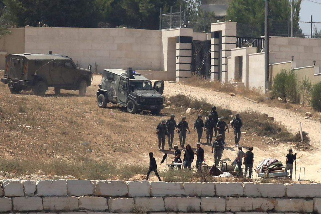 Israeli soldiers stand guard next to settlers in front of Palestinian homes that they have blockaded in the village of Qusra, south of Nablus, in the occupied West Bank, Wednesday, Aug. 12, 2026. (AP Photo/Nidal Eshtayeh)