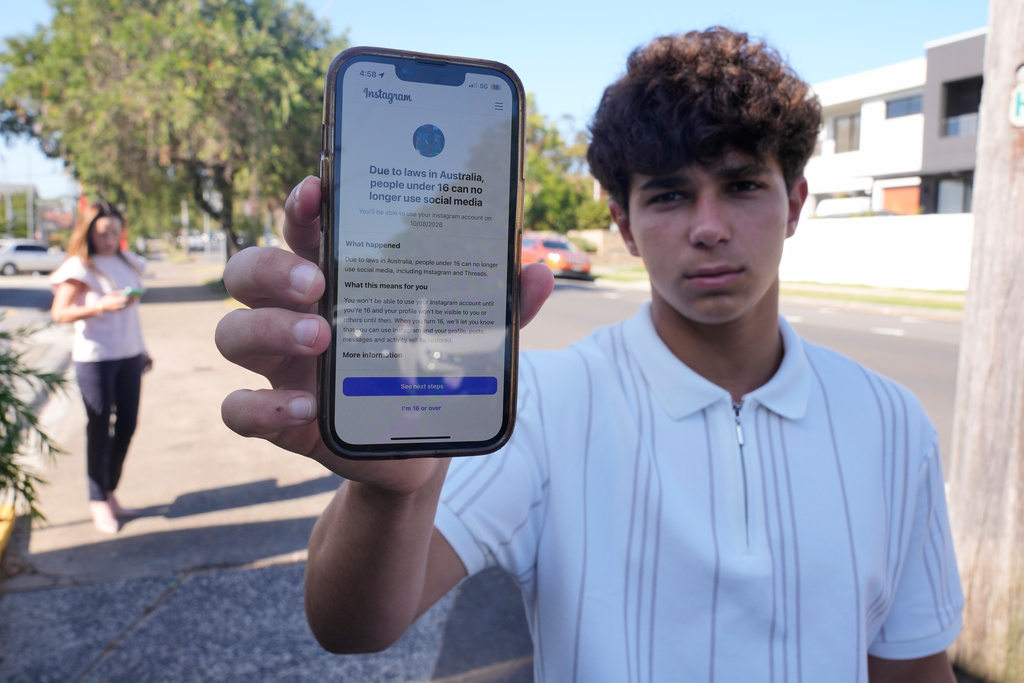 Noah Jones shows a warning on his phone that says he cannot access a social media site as his mother Renee, walks toward him in Sydney, Tuesday, Dec. 9, 2025. (AP Photo/Rick Rycroft)