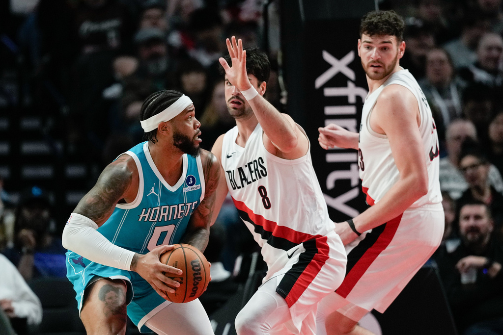 Charlotte Hornets forward Miles Bridges (0) looks to get around Portland Trail Blazers forward Deni Avdija (8) and center Donovan Clingan during the first half of an NBA basketball game Tuesday, March 10, 2026, in Portland, Ore. (AP Photo/Jenny Kane)