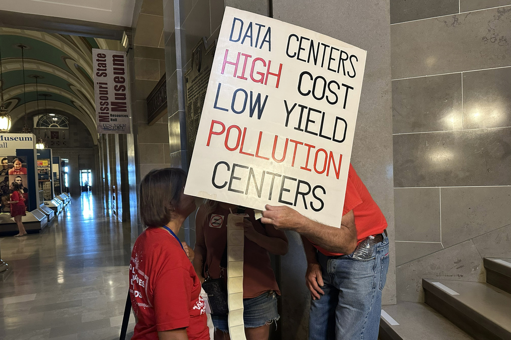 This photo taken with a smartphone shows opponents of data centers conversing behind a sign while preparing for a rally Wednesday, Sept. 16, 2026 at the Missouri Capitol in Jefferson City, Mo. (AP Photo/David A. Lieb)