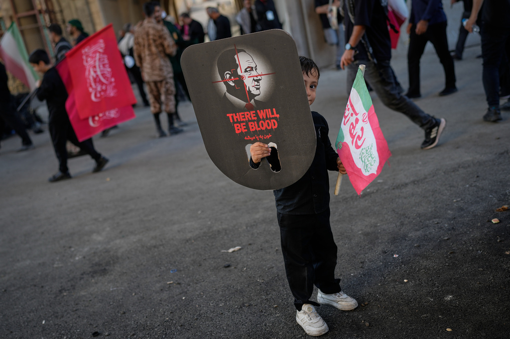 A boy peeks from behind a sign depicting Israel's Prime Minister Benjamin Netanyahu overlaid with crosshairs and the words "There will be blood" during funeral ceremonies for slain Iranian Supreme Leader Ayatollah Ali Khamenei and members of his family at the Imam Khomeini Mosalla Grand Mosque in Tehran, Iran, Sunday, July 5, 2026. (AP Photo/Altaf Qadri)