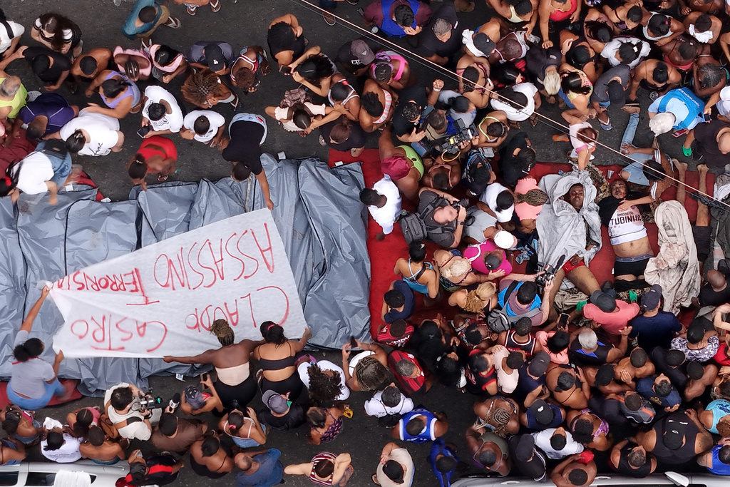 Residents gather around the bodies of men killed in a police raid targeting the Comando Vermelho gang the day before, next to a banner reading "Claudio Castro Murderer," referring to Rio de Janeiro state Governor Claudio Castro, in the Complexo da Penha favela of Rio de Janeiro, Brazil, Wednesday, Oct. 29, 2025. (AP Photo/Silvia Izquierdo)