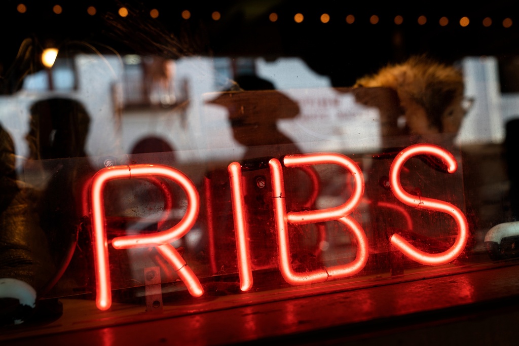 FILE - A neon sign advertises ribs at a steakhouse restaurant as pedestrians are reflected walking by in Fort Worth, Texas, April 21, 2023. (AP Photo/David Goldman, File)