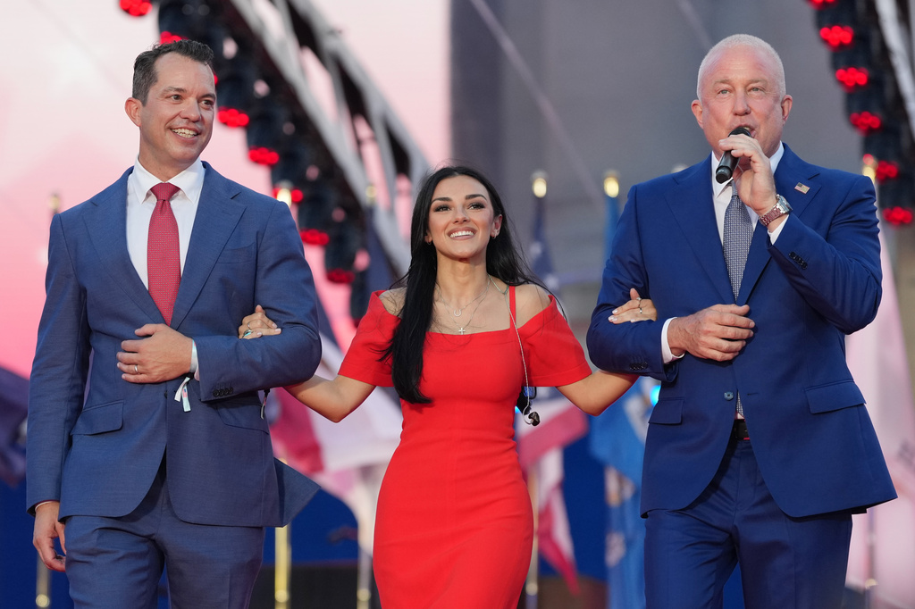 U.S. Ambassador to Belgium Bill White, right, and his husband Bryan Eure, left, walk U.S. country music singer Alexis Wilkins onto the stage during the America 250 event in Brussels, Sunday, June 28, 2026. (AP Photo/Virginia Mayo)