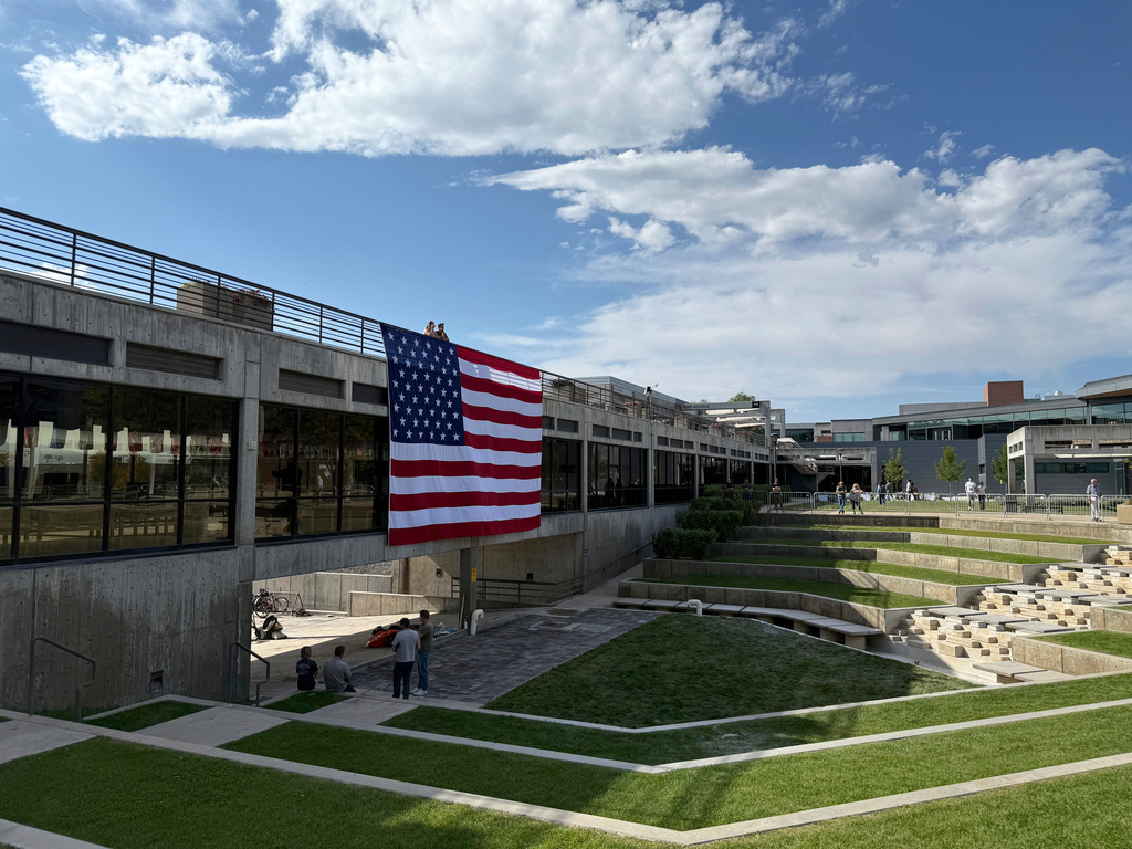 FILE - People gaze down at the site where Charlie Kirk was shot, above which hangs an American flag, at Utah Valley University, Sept. 15, 2025, in Orem, Utah. (AP Photo/Jesse Bedayn, File)
