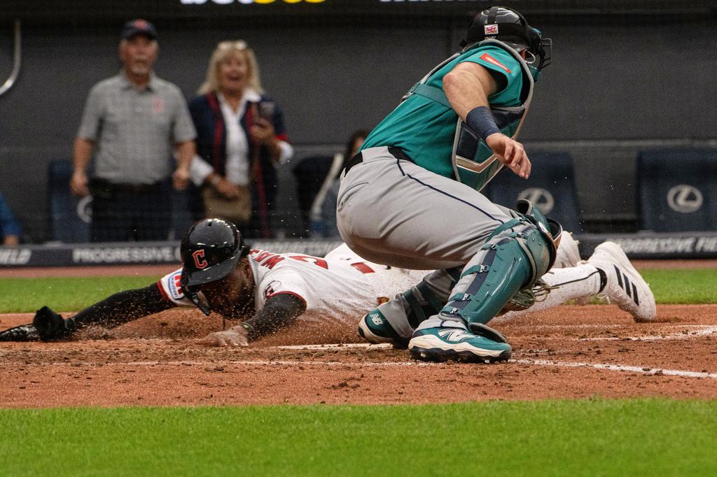 Seattle Mariners' Cal Raleigh, front, is late with the tag as Cleveland Guardians' Kahil Watson, left, slides safely into home plate on a two-run single by Guardians' Cooper Ingle during the third inning of a baseball game, Saturday, June 27, 2026, in Cleveland. (AP Photo/Phil Long) CORRECTION: Corrects to a two-run single not an RBI single.