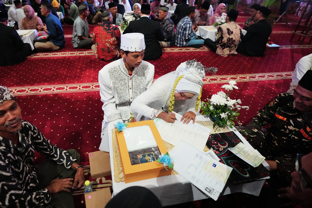 A bride signs her wedding certificate as the groom looks on during a mass wedding ceremony at Istiqlal Mosque in Jakarta, Indonesia, Wednesday, Dec. 3, 2025. (AP Photo/Tatan Syuflana)