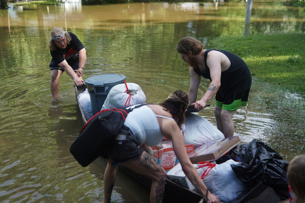 Scott Conrad, left, Joseph Workman, right, and Kesley Patterson, back to camera, push a kayak through floodwaters as they transport items from their flooded homes in Indianapolis, Sunday, Aug. 16, 2026. (AP Photo/Obed Lamy)