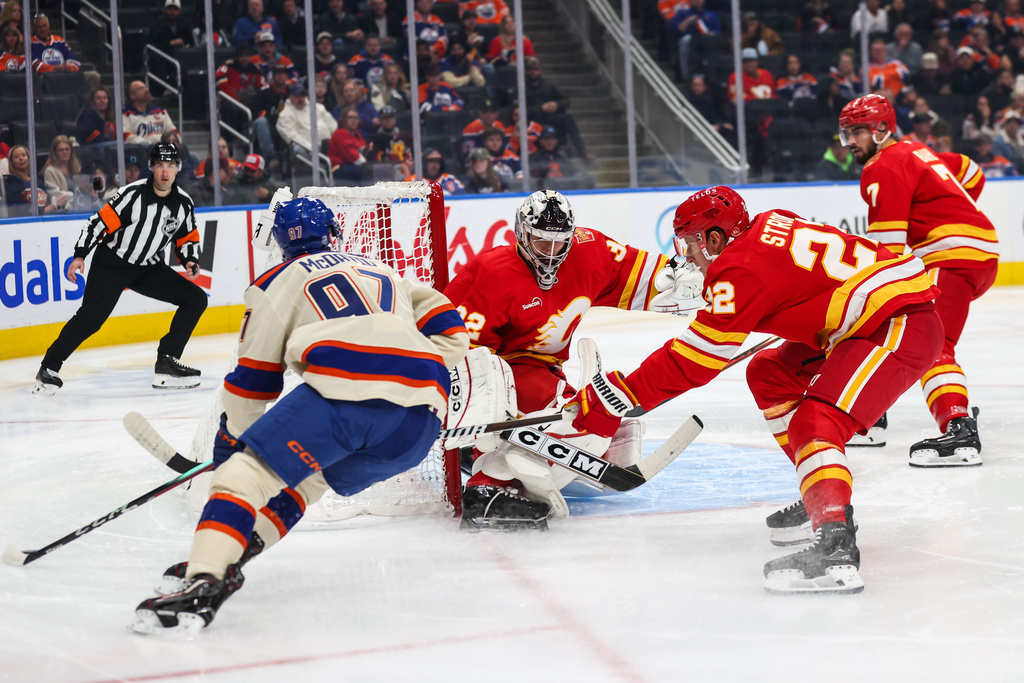 Edmonton Oilers' Connor McDavid, left, looks for an opportunity against Calgary Flames goaltender Dustin Wolf, center, during the second period of an NHL hockey game in Edmonton, Alberta, Wednesday, Oct. 28, 2026. (Codie McLachlan/The Canadian Press via AP)