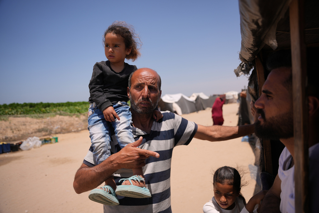 Ne'man Abu Jarad carries his granddaughter Hour Abu Jarad as he talks with a neighbor at a tent camp for displaced Palestinians in Khan Younis, southern Gaza Strip, Wednesday, May 13, 2026. (AP Photo/Abdel Kareem Hana)