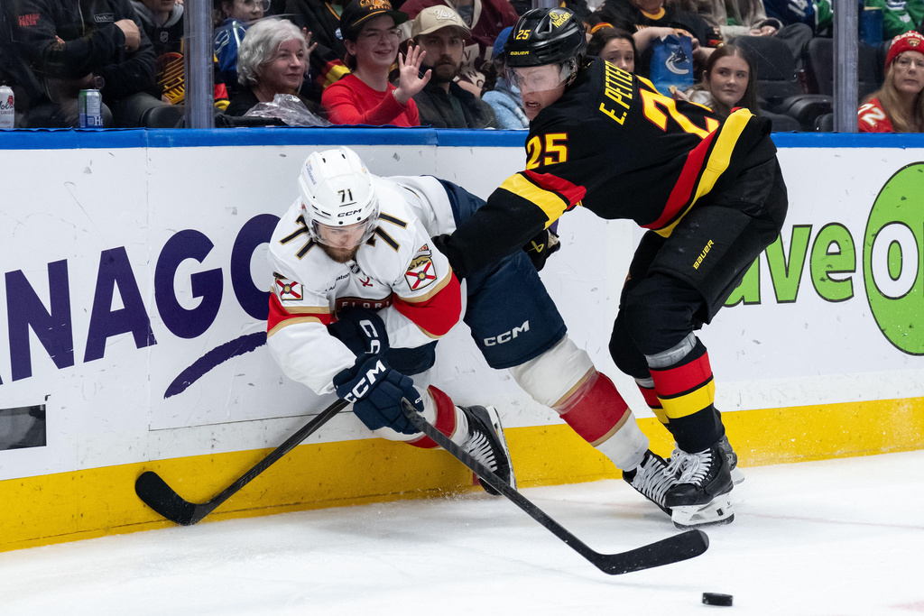Florida Panthers' Luke Kunin passes the puck as he is hit by Vancouver Canucks' Elias Pettersson (25) during the second period of an NHL hockey game in Vancouver, on Tuesday, March 17, 2026. (Ethan Cairns/The Canadian Press via AP)
